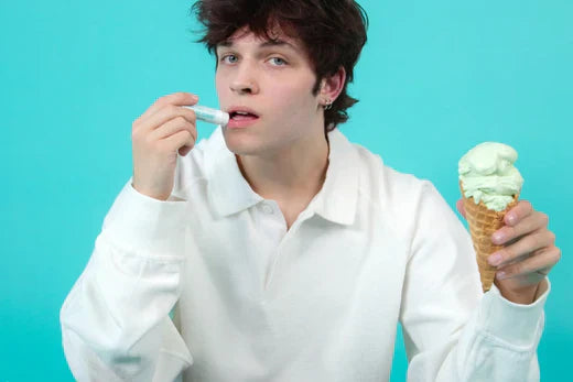 Mint lip balm applied by a young man holding a mint ice cream cone against a turquoise background.