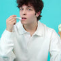 Mint lip balm applied by a young man holding a mint ice cream cone against a turquoise background.