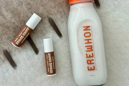 Space Camp Coconut Cream organic lip balms displayed alongside an Erewhon coconut milk bottle on a soft textured surface