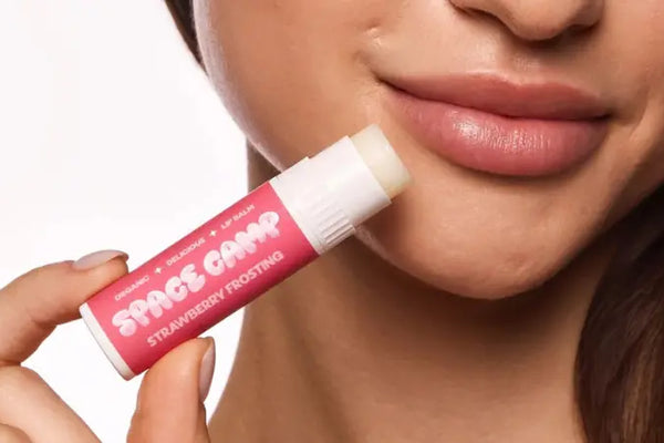 Lip care labeled Strawberry Frosting held near a woman's smooth, moisturized lips.