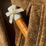 Best natural lip balm with caramel flavor, decorated with a bow, tucked into the pocket of a brown suede jacket.