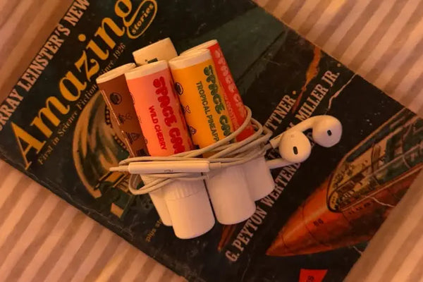 Hydrating lip care featuring multiple flavors of "Space Camp" lip balm wrapped with earphones on a vintage sci-fi book.