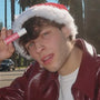 Natural lip balm held by a man in a Santa hat and red jacket posing outdoors with palm trees in the background.
