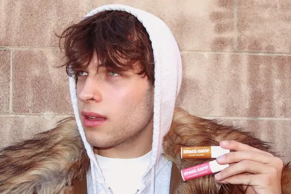 Natural lip hydration with salted caramel and wild cherry lip balms held by a stylishly dressed person in a fur-lined hoodie