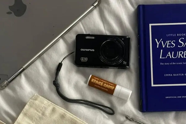 Organic lip balm with a salted caramel flavor displayed on a neatly arranged bed featuring a book, camera, and tablet.