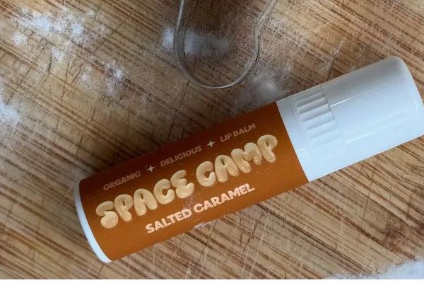 Organic lip balm in a salted caramel flavor, placed on a wooden surface with scattered flour and a metal cookie cutter.