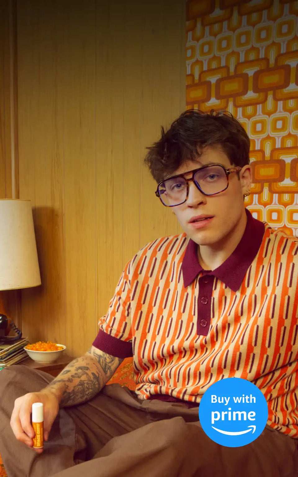  Man wearing retro glasses and a vintage patterned shirt, holding a lip balm in a room with 70s-style decor