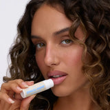 A person with curly hair applying Space Camp Birthday Cake organic chapstick in a close-up portrait.