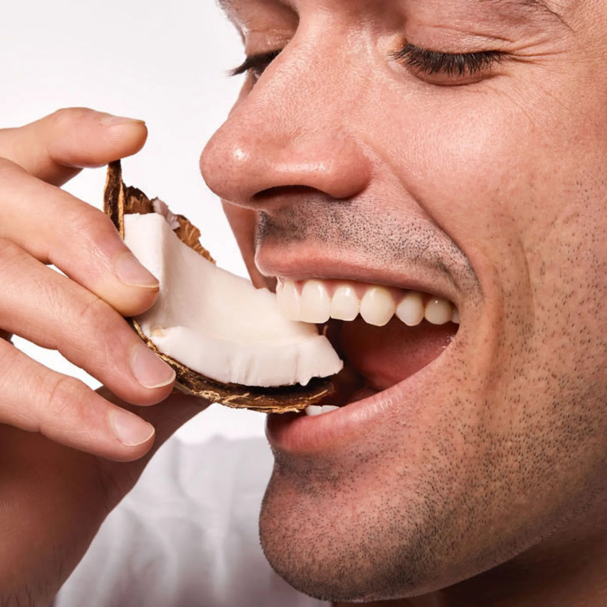 Close-up of a man biting into a fresh coconut, evoking the tropical coconut flavor of Space Camp Coconut Cream Lip Balm.
