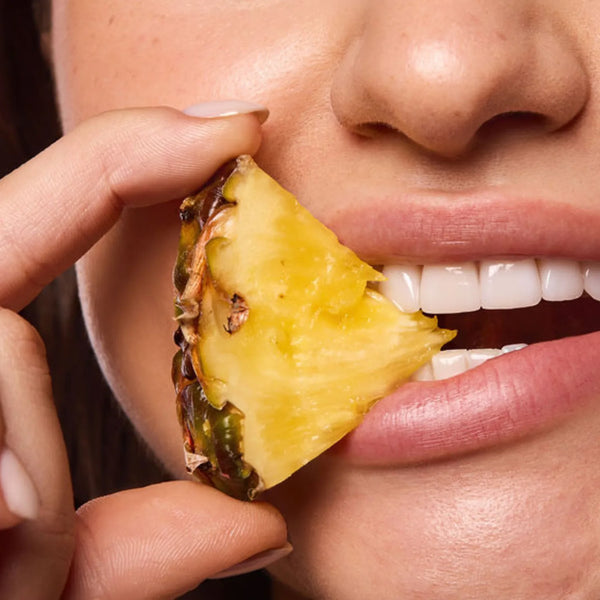 Close-up of lips biting into a fresh pineapple wedge, evoking the tropical flavor of Space Camp Tropical Pineapple Lip Balm.