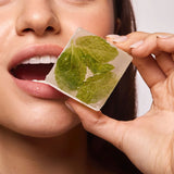 Close-up of lips holding a frosted ice cube with fresh mint leaves, evoking the cooling flavor of Space Camp Frosted Mint Lip Balm.