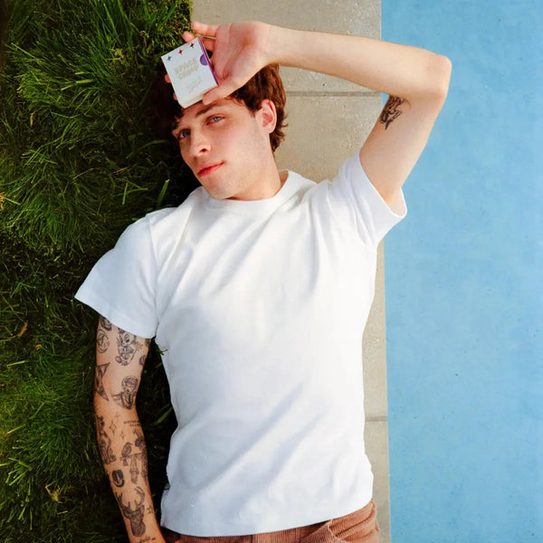 Person lying on grass by a pool holding a Space Camp Kool-Aid lip balm box.