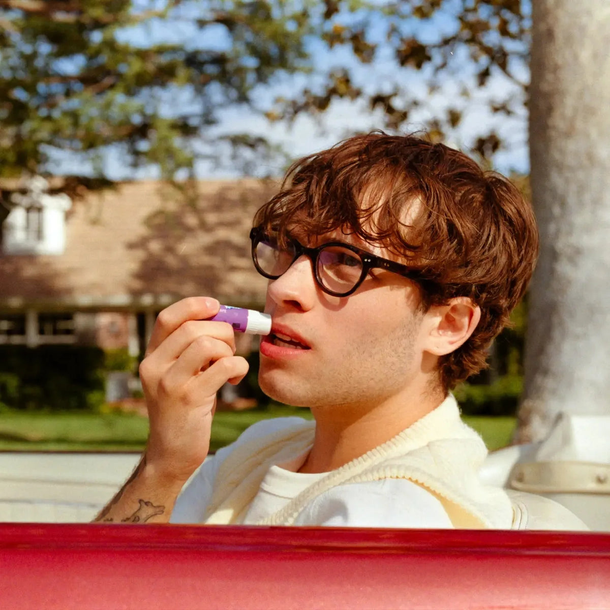 Person applying purple Kool-Aid flavored lip balm outdoors in warm sunlight.