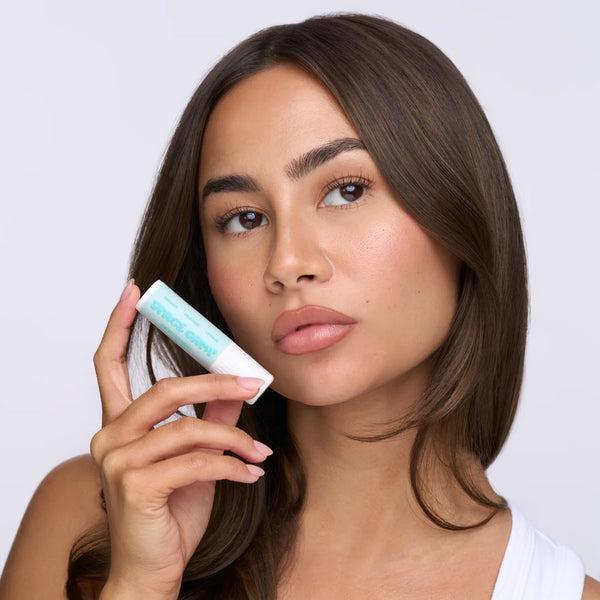 Woman with brown hair holding Space Camp Frosted Mint organic lip balm near her face against a neutral background.